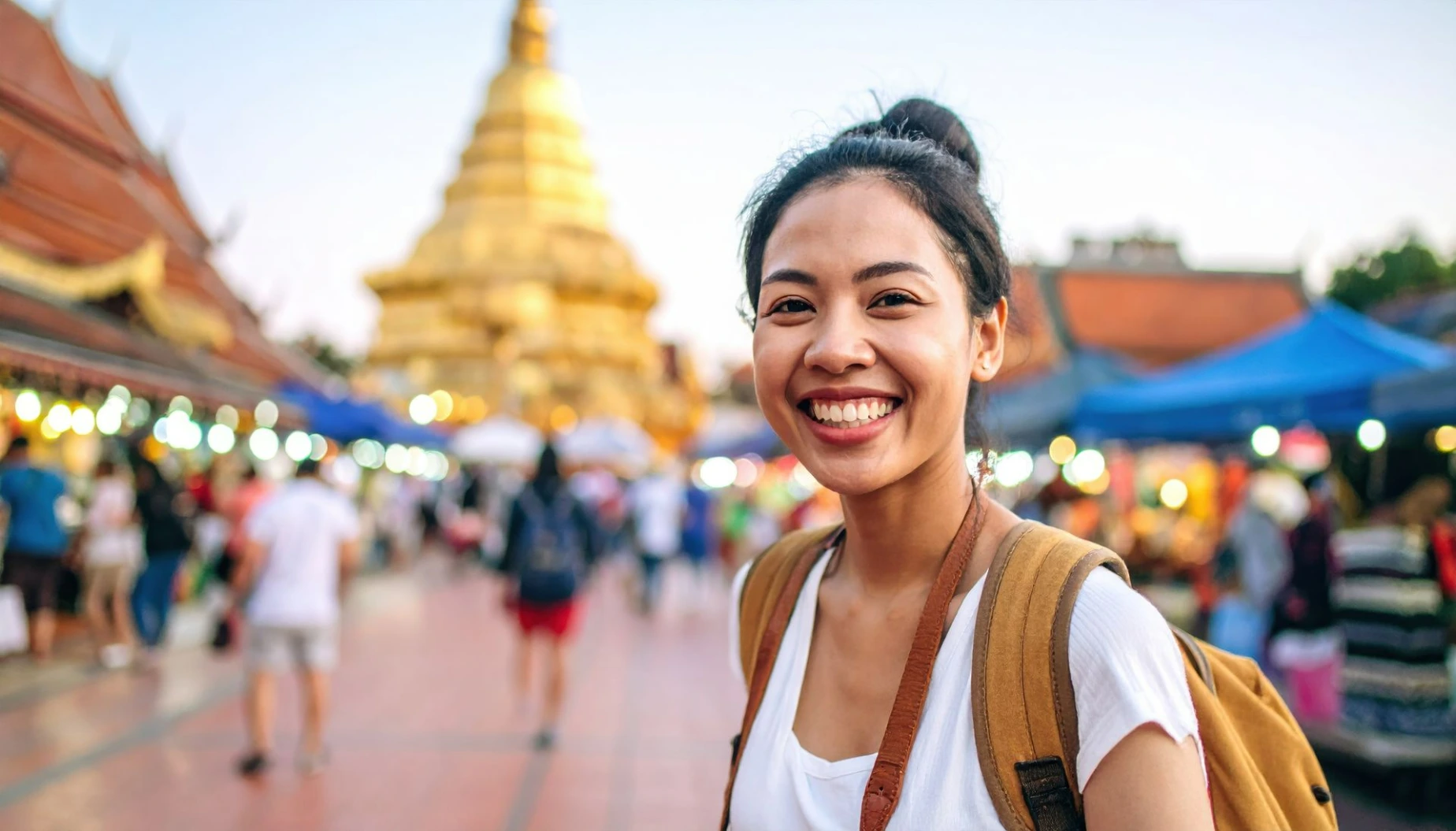 Smiling traveler enjoys vibrant atmosphere of bustling market, with golden temple in background, capturing essence of adventure and joy