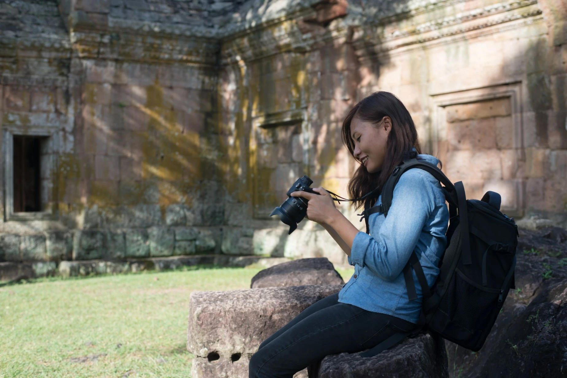 Young attractive woman photographer tourist with backpack coming to shoot photo at ancient phanom rung temple in Thailand.
