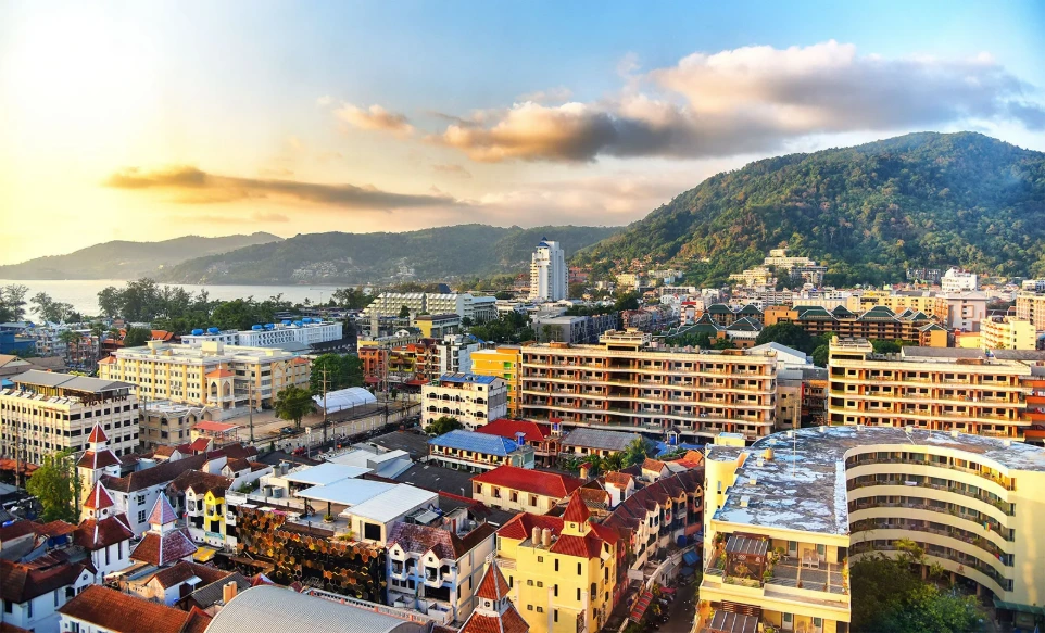 Panoramic view captures Patong town and bay in Phuket, Thailand, showcasing the dense mix of hotels and residential blocks nestled against the lush green hills during golden hour.