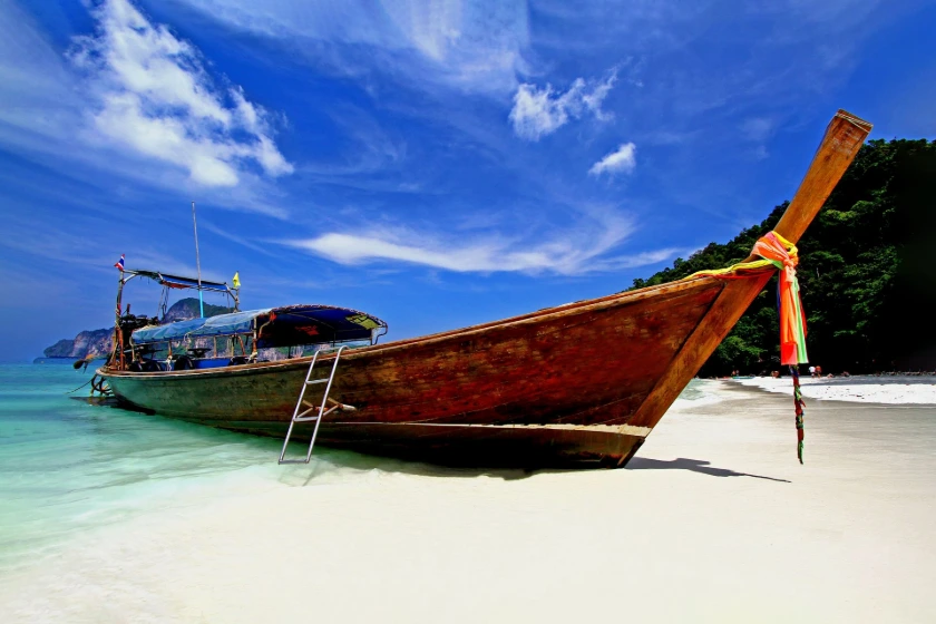 Big long tail boat parking on the white sand beach with blue sky and white clouds at Phi Phi island Krabi, Thailand